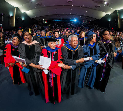Guests at Charter Day Convocation holding hands to sing alma mater